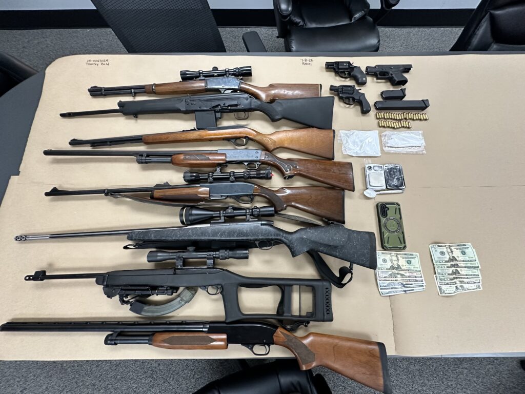 11 guns (rifles & handguns), money, bullets and drug paraphernalia displayed on a table